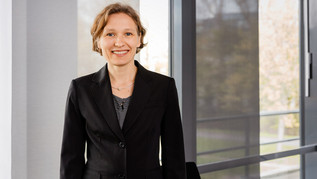 A middle-aged woman is standing in front of a window.