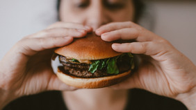 A person holds a burger in front of his face. 