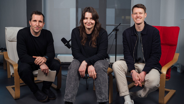 In der Mitte sitzt eine junge schwarzhaarige Frau, rechts und links von ihr jeweils ein junger Mann.
